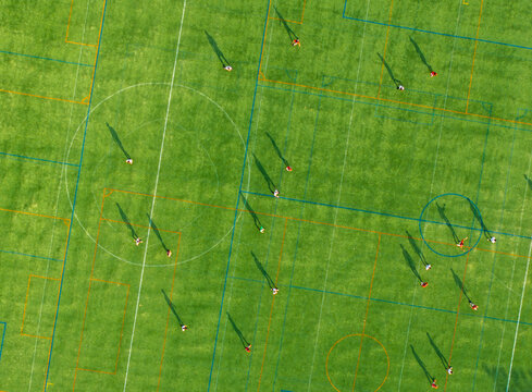 Aerial view of players scattered across the verdant field, their shadows stretching long under the sun, creating a dynamic contrast of light and shade, Brooklyn, New York, United States.