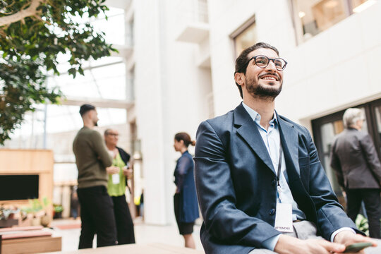 Low angle view of happy male business expert day dreaming while sitting in congress center lobby