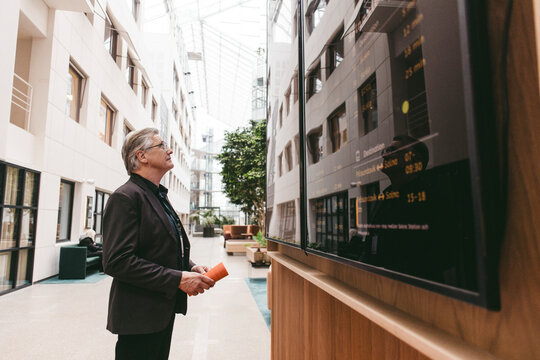 Side view of senior male business professional reading board at convention center lobby