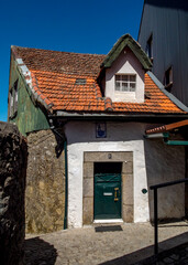 A small, old building with a red-tiled roof and a green door.