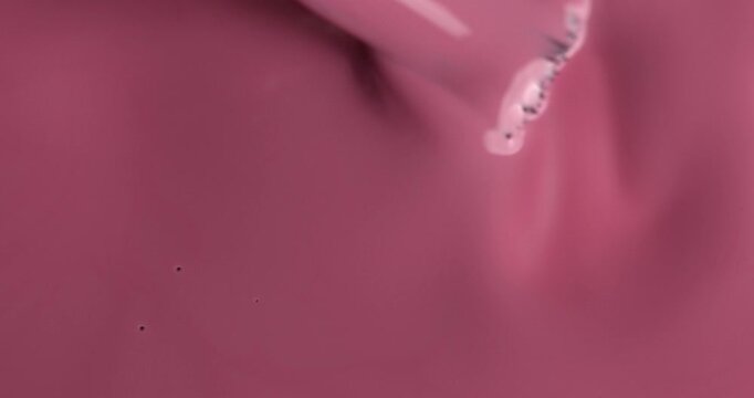Liquid nail polish surface, pink nail polish is applied with a brush manicure concept, slow motion. Manicure salon, nail polish texture, background. Top view.