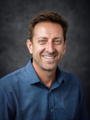 Obraz premium Smiling man wearing a blue dress shirt poses in front of a gray background during the daytime