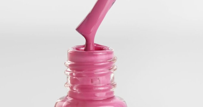 Pink nail polish dripping from a brush into a bottle, close-up footage.