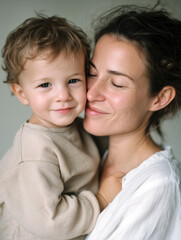 Close-up portrait of a loving middle-aged mother holding her young son cheek to cheek, both smiling and only boy looking at the camera, capturing a warm, affectionate family moment.