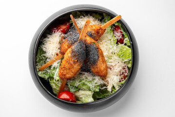 Caesar salad with romaine lettuce, cherry tomatoes, Parmesan, and three skewers of breaded fried chicken, garnished with seasoning. Served in a bowl, top view, isolated on white.
