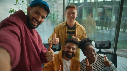 Web cam POV four multiracial colleagues informal business team making selfie photo posing together happy smiling showing thumbs up casual corporate friends in coworking office video call live vlog