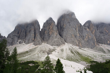 Majestic Dolomite mountains shrouded in clouds with lush green forest in the foreground and rocky terrain