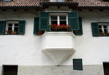 Charming white house with green shutters and flower-filled balcony in a picturesque European village setting