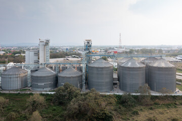 Industrial Grain Silos under Cloudy Sky: The imposing industrial grain silos stand tall beneath a cloudy sky, embodying the scale and efficiency of modern agricultural storage.