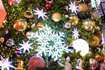 close up multicolor decoration ball with snow star and light bulb on Christmas tree pile tree at night time on holiday snowy xmas theme in december 