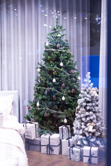 A white winter snow CHRISTMAS TREE with surrounded gift box present beside bed in the house. Home in holiday