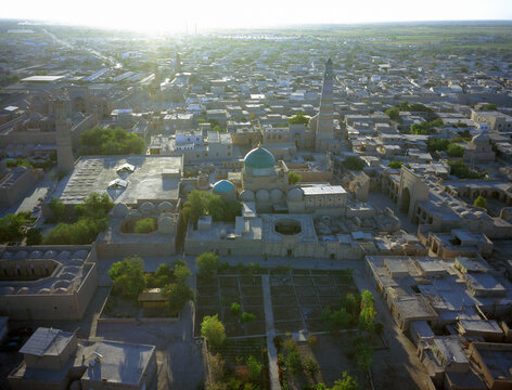Aerial view of ancient architecture with turquoise domes and towering minarets basks in the warm glow of the setting sun, Khiva, Uzbekistan.