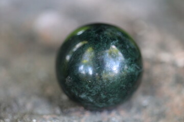 A single green marble ball sits on the ground, often used as a decorative element or in still life photography