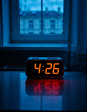 Digital alarm clock displaying 4:26 in a dark room with a window view