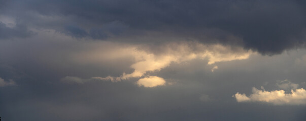 Fototapeta premium Large gray storm clouds with golden sun rays shining through them, creating a dramatic and gloomy atmosphere
