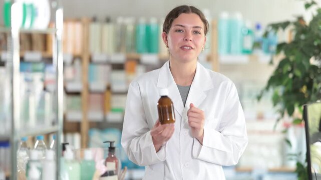 Female pharmacist standing near counter in pharmacy and offering medicated throat syrup. High quality 4k footage