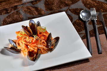pasta with mussels and vegetables in a white plate on a dark background