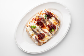 Gourmet open-faced sandwich with melted cheese, grilled meat, caramelized onions, and fresh basil on toast. Served on white plate, isolated on white background