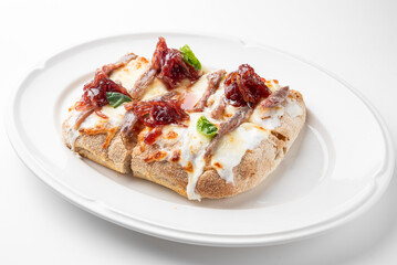Gourmet open-faced sandwich with melted cheese, grilled meat, caramelized onions, and fresh basil on toast. Served on white plate, isolated on white background