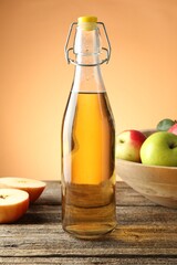 Delicious cider in glass bottle and apples on wooden table against orange gradient background