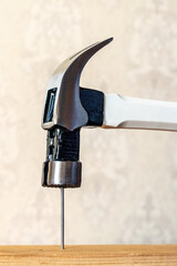 A metal hammer with a white handle drives a nail into a wooden board, illustrating the process of construction and working with tools