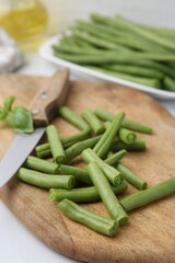Cut green bean pods and knife on white table, closeup
