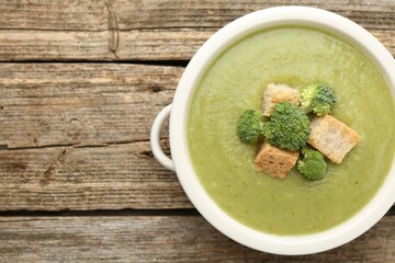 Tasty broccoli cream soup with croutons in bowl on wooden table, top view. Space for text