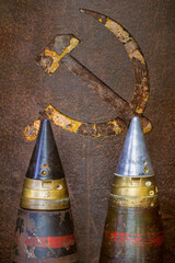 Two old military bombs in front of a weathered USSR hammer and sickle