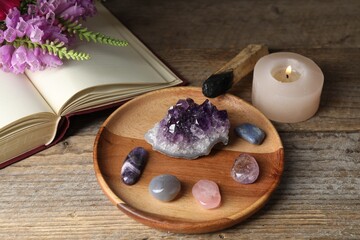 Different beautiful gemstones, book, flowers, palo santo and burning candle on wooden table, closeup