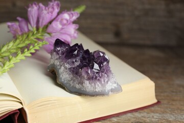 Beautiful amethyst gemstone, flowers and book on wooden table, closeup