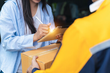 Woman Signing For Package Delivery While Receiving Box From Courier In Uniform Outside Home During Daylight Capturing Modern Logistics Concept