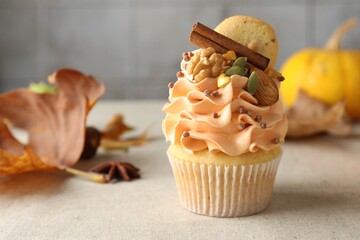 Delicious cupcake with color cream, spices, cookie, nuts and autumn decor on grey table, closeup