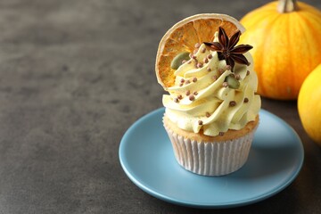 Delicious cupcake with color cream, anise, dried orange and autumn decor on grey table, closeup. space for text
