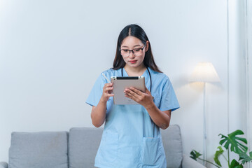 Young female healthcare professional in scrubs using tablet device in modern home environment while looking focused on the screen