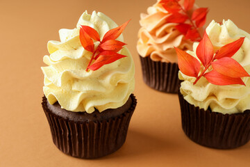 Delicious cupcakes with branches with red leaves on coral background, closeup. Autumn atmosphere