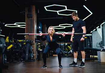 Woman squatting with barbell in gym with trainer. Female athlete lifting barbell under supervision of personal trainer in fitness club.