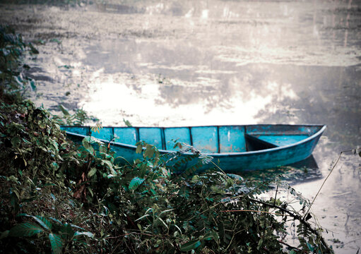 Rustic Blue Wooden Boat Moored on a Lush Green Shore with Calm Reflective Water in a Rural Landscape