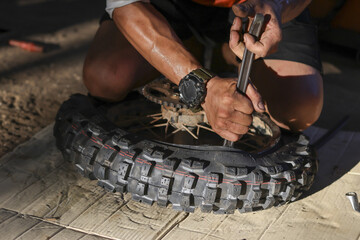 Man performing tire repair, using tool to change motorcycle wheel outdoors. Focused determination shines through during essential off road maintenance, task requiring significant effort