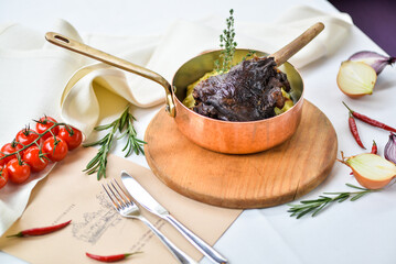 shank baked in a copper pan on a table with vegetables