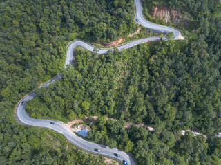 Winding road navigates dense mountain forest, presenting exciting aerial view for travelers seeking adventurous journeys nature. Lush green landscape evokes feeling of exploration and freedom