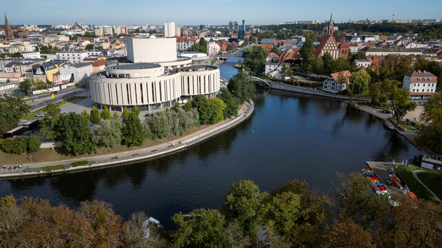 Aerial view of the Opera Nova's modern curves contrasting with the historic red-brick church along the dark, reflective Brda River, Bydgoszcz, Wojew&Atilde;&sup3;dztwo kujawsko-pomorskie, Poland.