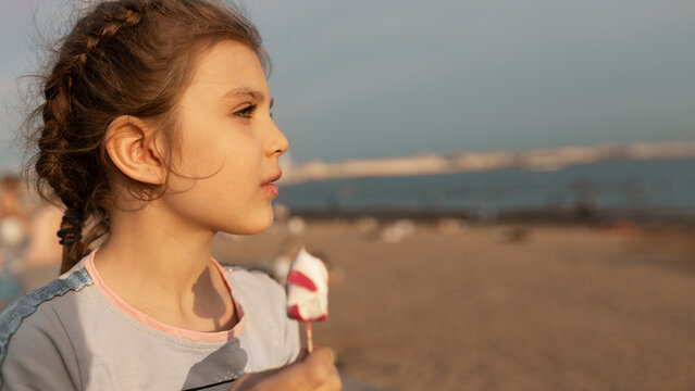 Portrait in profile girl 7 years old with ice cream, looking into the distance on the beach, banner