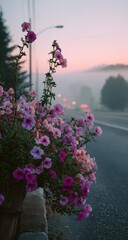 Vibrant pink and purple petunias in a roadside planter, softly illuminated by the dusky sunrise light, with a misty highway receding into the background