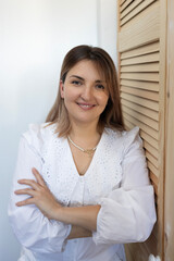 Smiling woman in white blouse with arms crossed standing by wooden wall in bright indoor space
