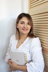 Smiling woman holding a planner while standing near wooden slats in a bright, cozy indoor space