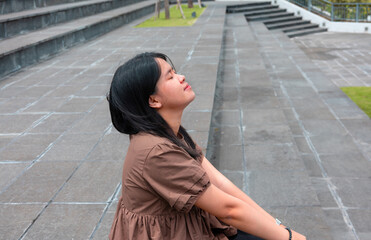 Fototapeta premium Young Asian woman smiling happily while relaxing in a green space. Beautiful lifestyle, enjoy life, green life, wellbeing concept, sustainable development. Stock photo