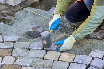 Laborer carefully places cobblestones levels sand for new pathway at construction site on work day.