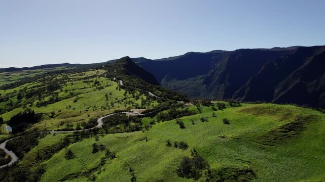 Cinematic drone orbit over a sinuous road climbing along a valley on Reunion Island. Clear skies and panoramic views highlight the dramatic landscape.