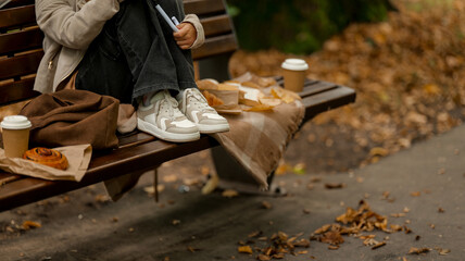 Person relaxing on a park bench with coffee and pastry in autumn