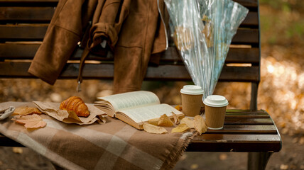 Autumn picnic scene on a park bench with coffee, a book, and a croissant.